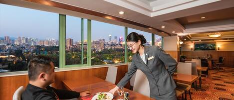 A hotel room with a city view, a dining area, and a reception desk.