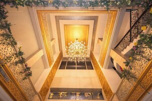 Una imponente escalera con candelabro, diseños ornamentales en las paredes y decoración floral.