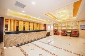 A hotel lobby with a reception desk, seating area, and a chandelier.