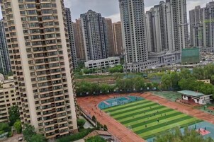Un edificio residencial alto con varios balcones, un campo deportivo y edificios altos circundantes.