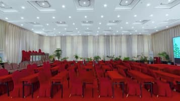 A conference room with rows of tables and chairs, a stage, and a large screen.