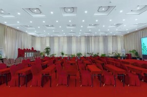 Un salón de conferencias con filas de mesas y sillas, un escenario y una pantalla grande.