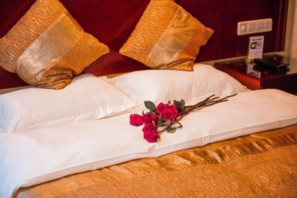 A bed with white linens, two golden pillows, and a bouquet of red roses.