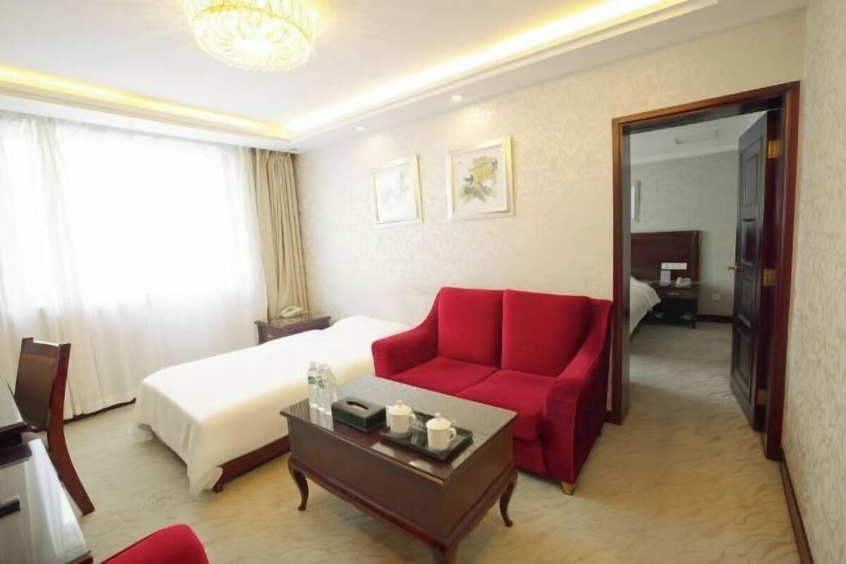 A hotel room with a bed, a red sofa, a wooden coffee table with a tray, and a mirror.