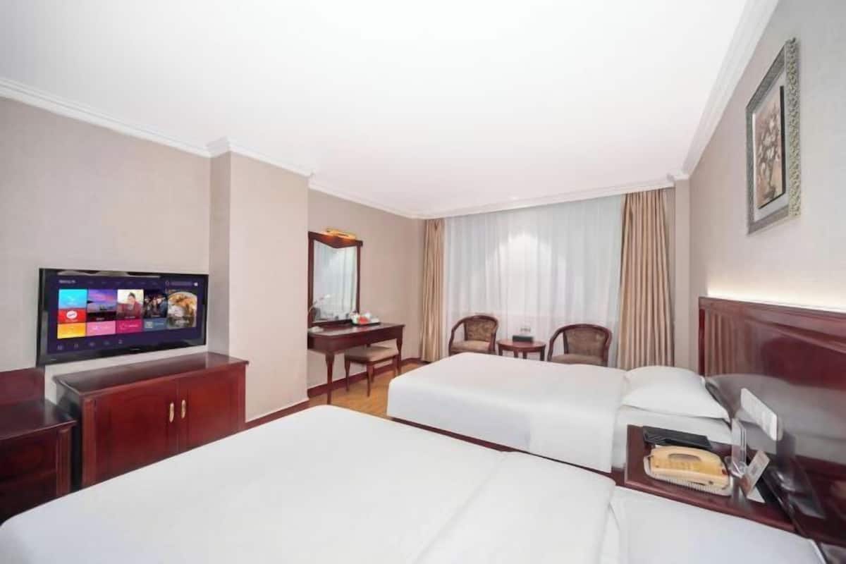 A hotel room with two beds, a desk, a television, and a telephone.