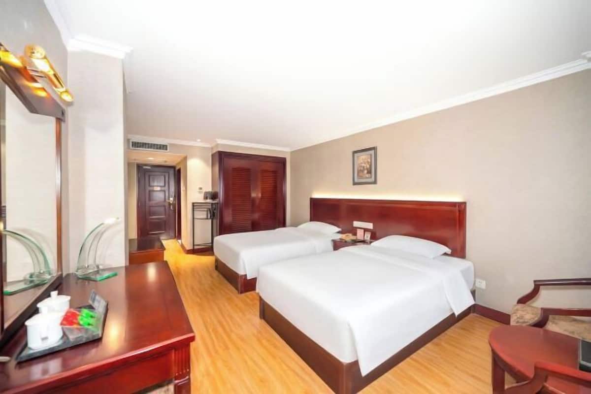 A hotel room with two beds, a desk with a tray of amenities, a mirror, and a door leading to a bathroom.