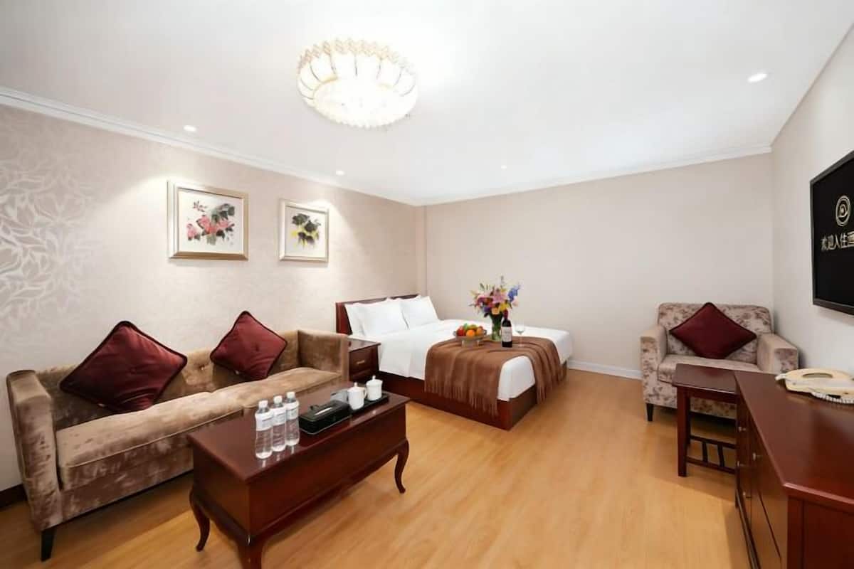 A hotel room with a bed, a sofa, a coffee table, a TV, and a chair.