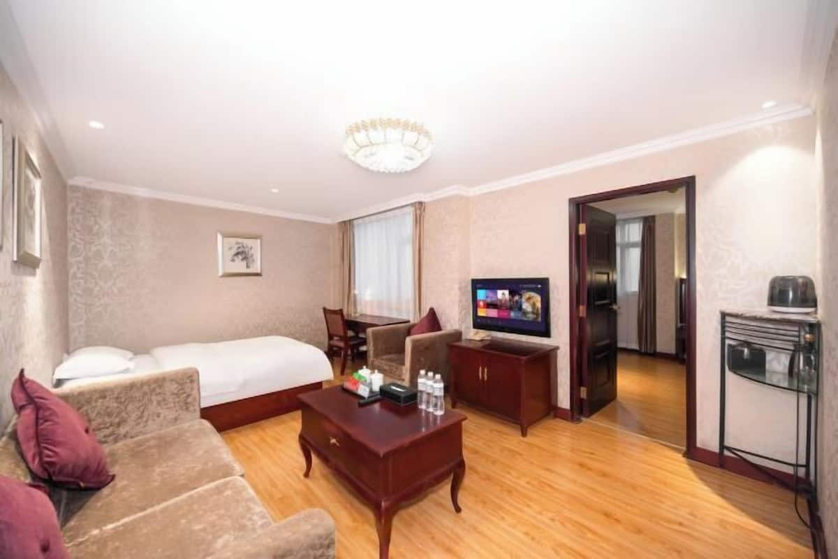 A hotel room with a bed, a sofa, a TV, a coffee table, and a small kitchenette.