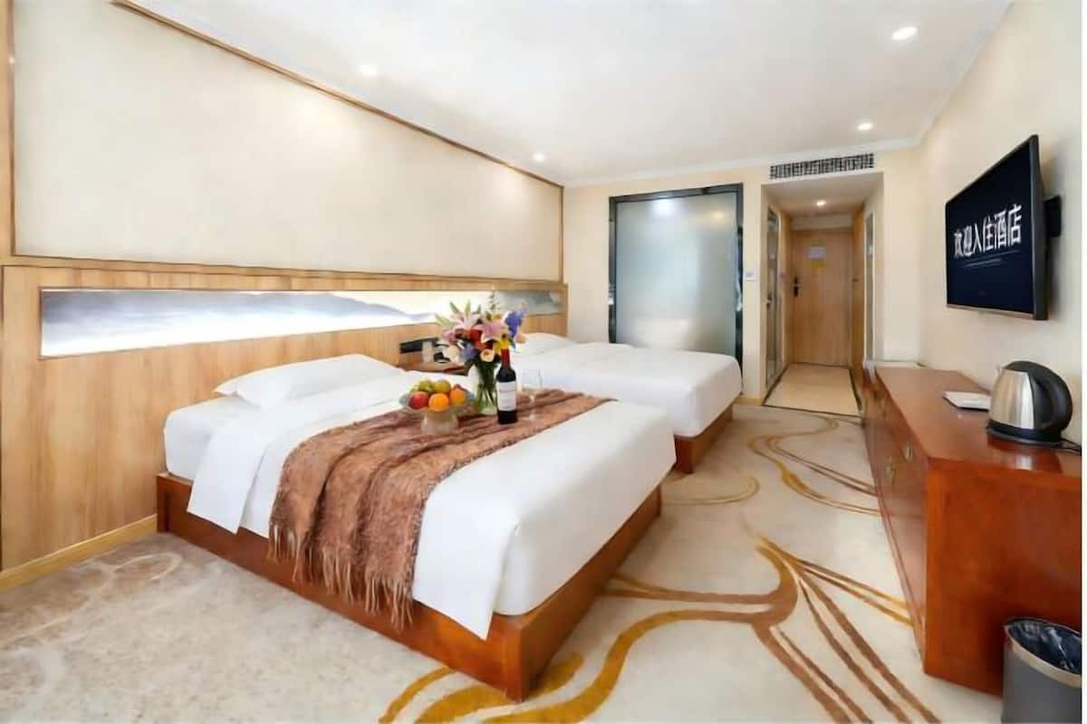 A hotel room with two beds, a desk, a TV, and a fruit bowl on the nightstand.