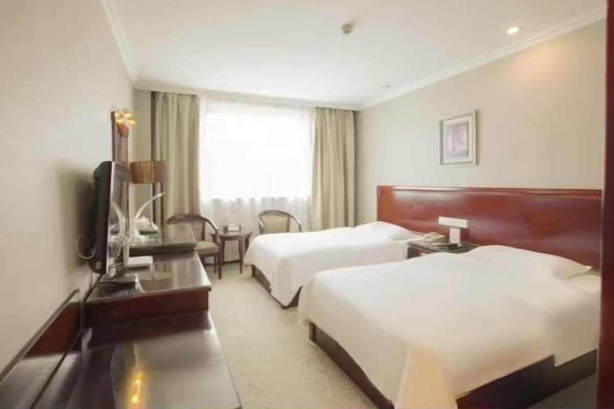 A hotel room with two beds, a desk, a chair, a TV, and a window with curtains.
