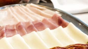 Eine Auswahl an Wurstwaren, darunter Salami und Prosciutto, auf einer Platte angerichtet. Im Hintergrund befindet sich eine Schale mit Tomatensauce und Brot.