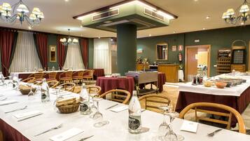 A hotel dining area with tables set for a meal, including wine glasses, bottles, and bread baskets.