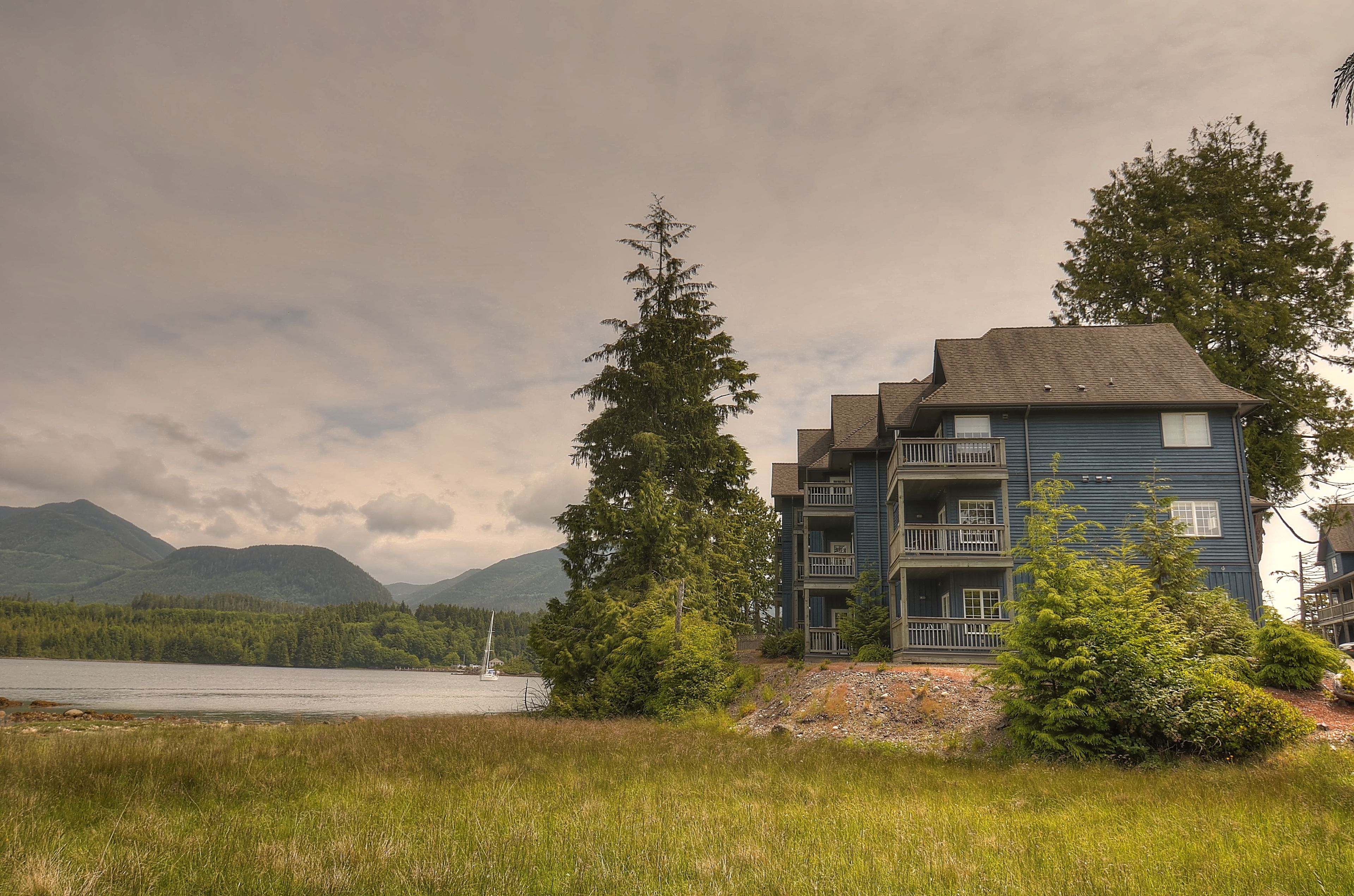 A two-story building with balconies, located near a lake with mountains in the background.