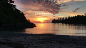 A sunset over a calm body of water with a rocky shoreline and trees in the background. - Waters Edge Shoreside Suites (Ucluelet)
