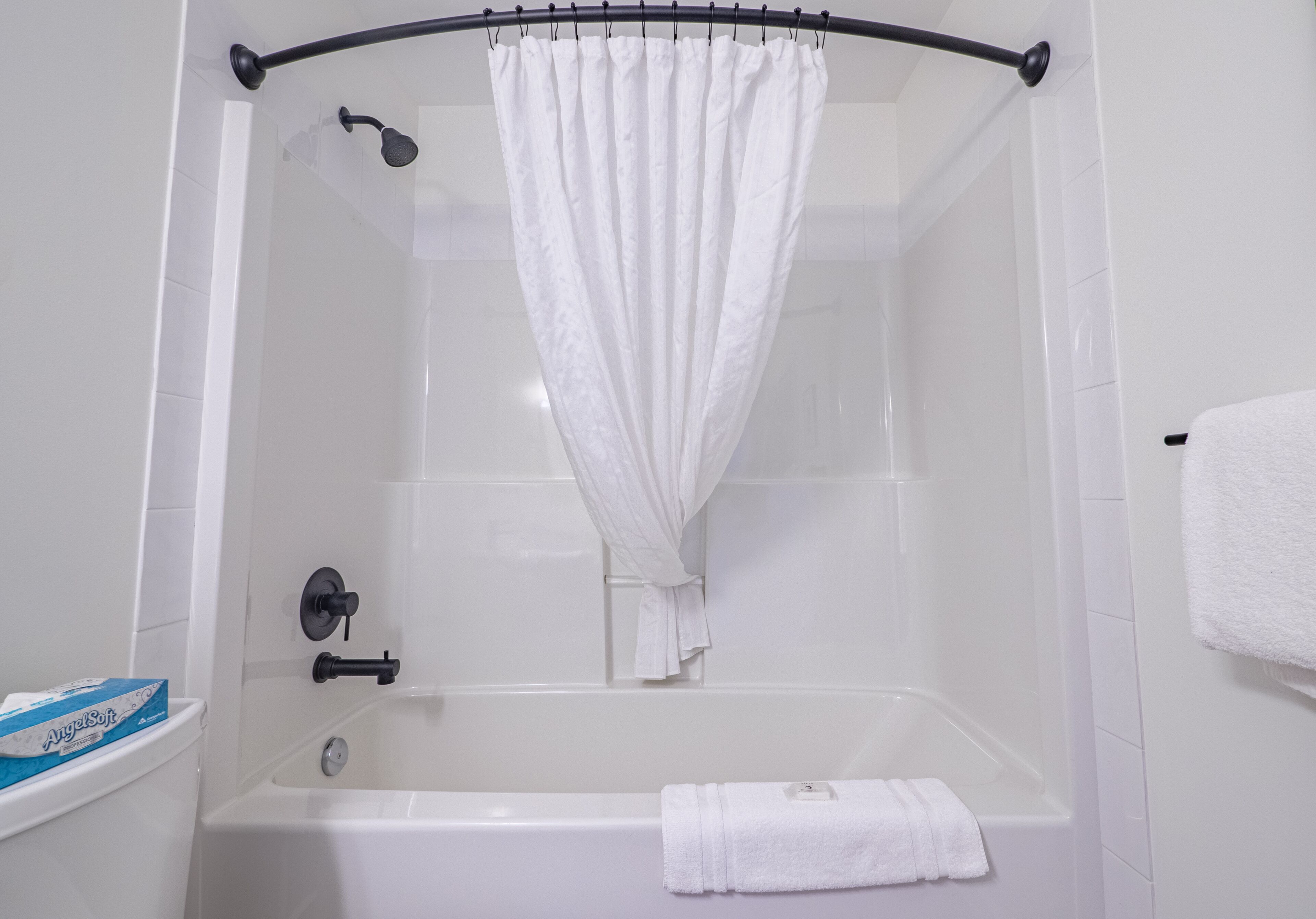 A white bathtub with a shower curtain, a towel, and a toilet with a box of toilet paper.