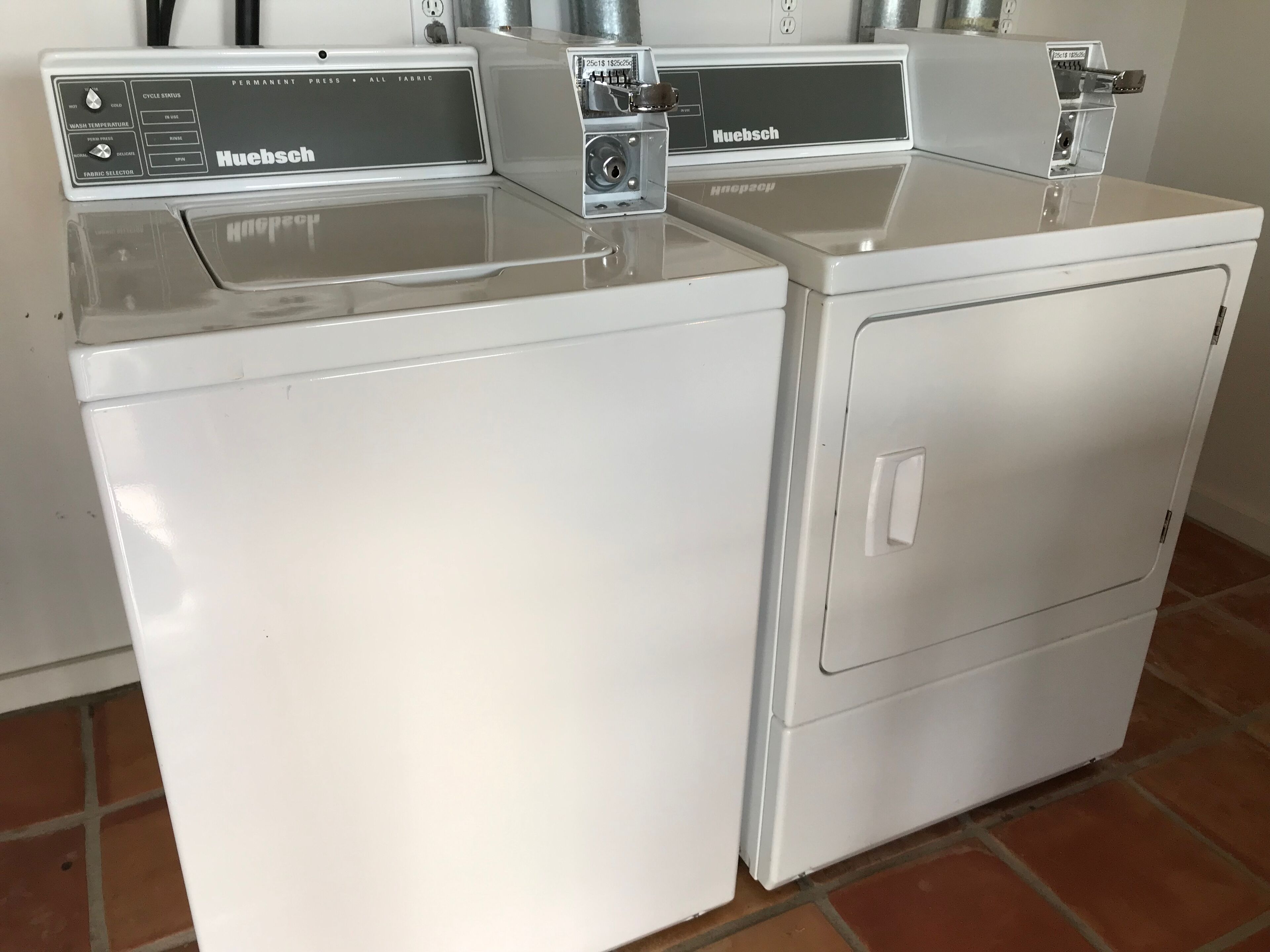 Two white Huebsch washing machines side by side in a room with tiled flooring.