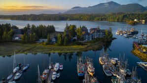 A marina with boats docked, surrounded by houses and a forested landscape with mountains in the background. - Waters Edge Shoreside Suites (Ucluelet)