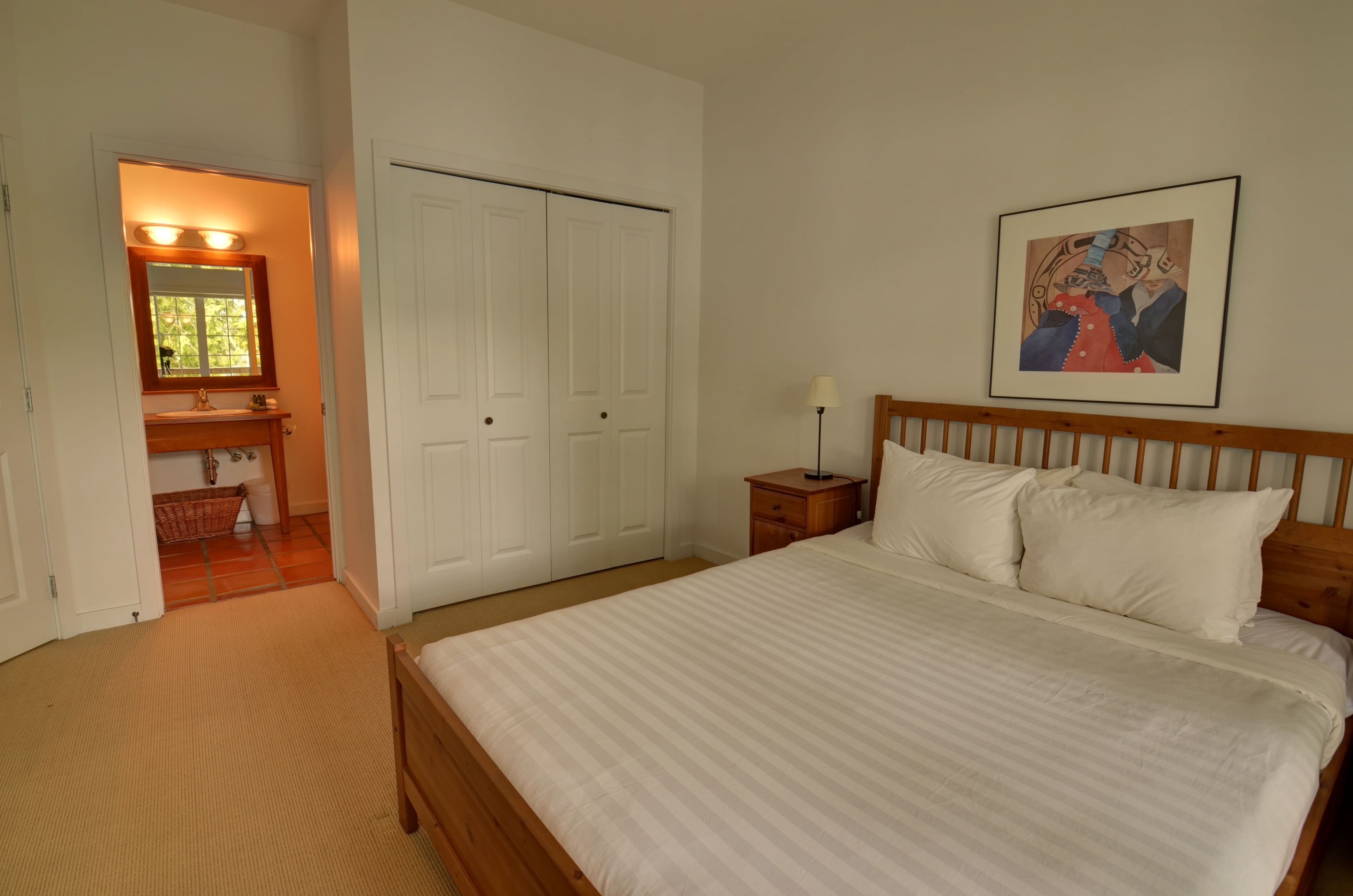 A bedroom with a bed, a nightstand, a wooden headboard, a framed picture, and a closet.