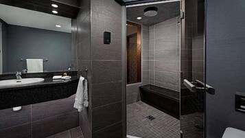 A modern bathroom with a dark tile design, a glass-enclosed shower, and a sink with a towel.
