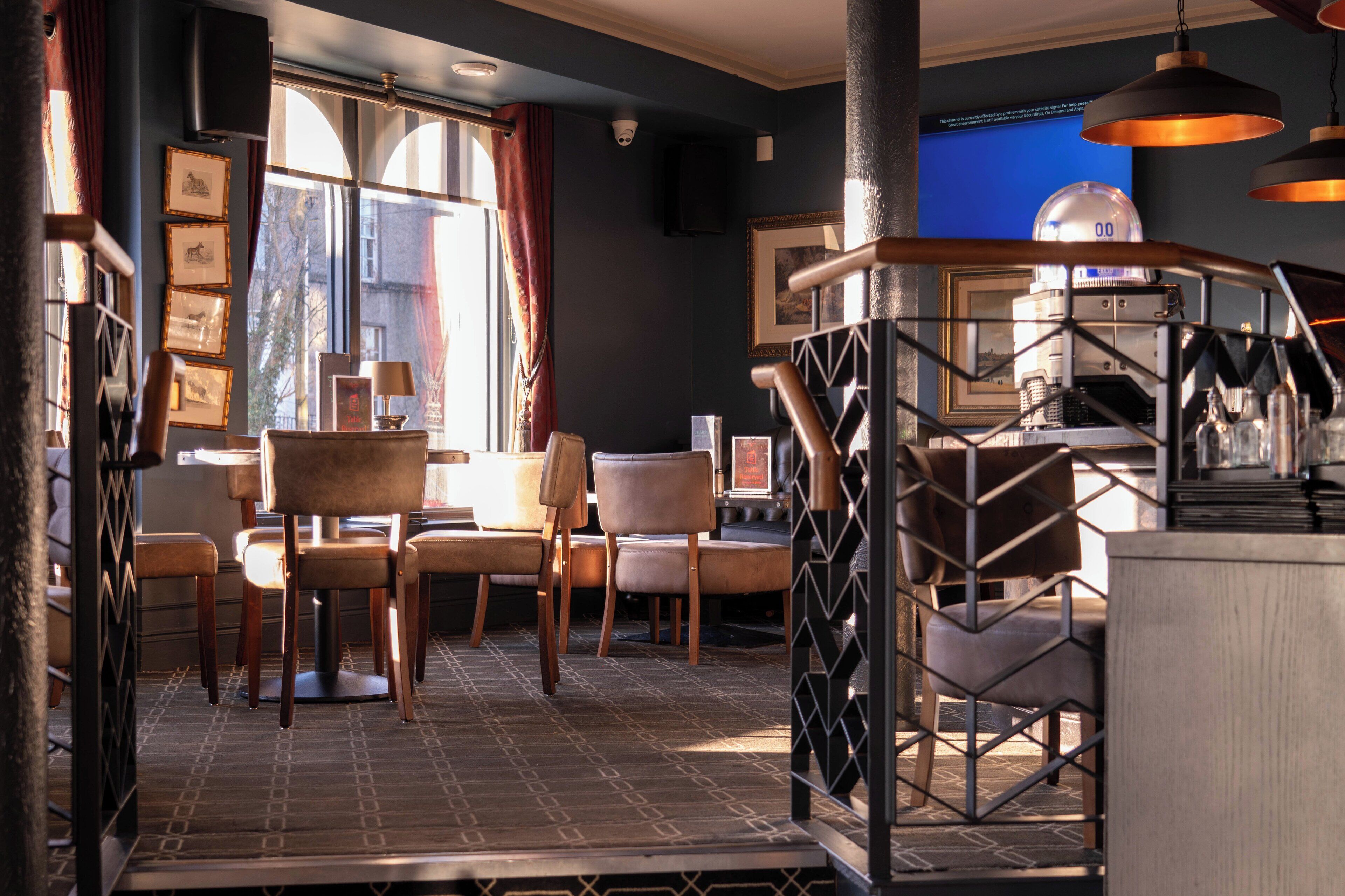 A modern interior with a dining area, wooden chairs, a staircase, and a view of the city through large windows.