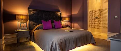 A bedroom with a large bed, two bedside tables with lamps, a headboard, and a shower area with a patterned wall.