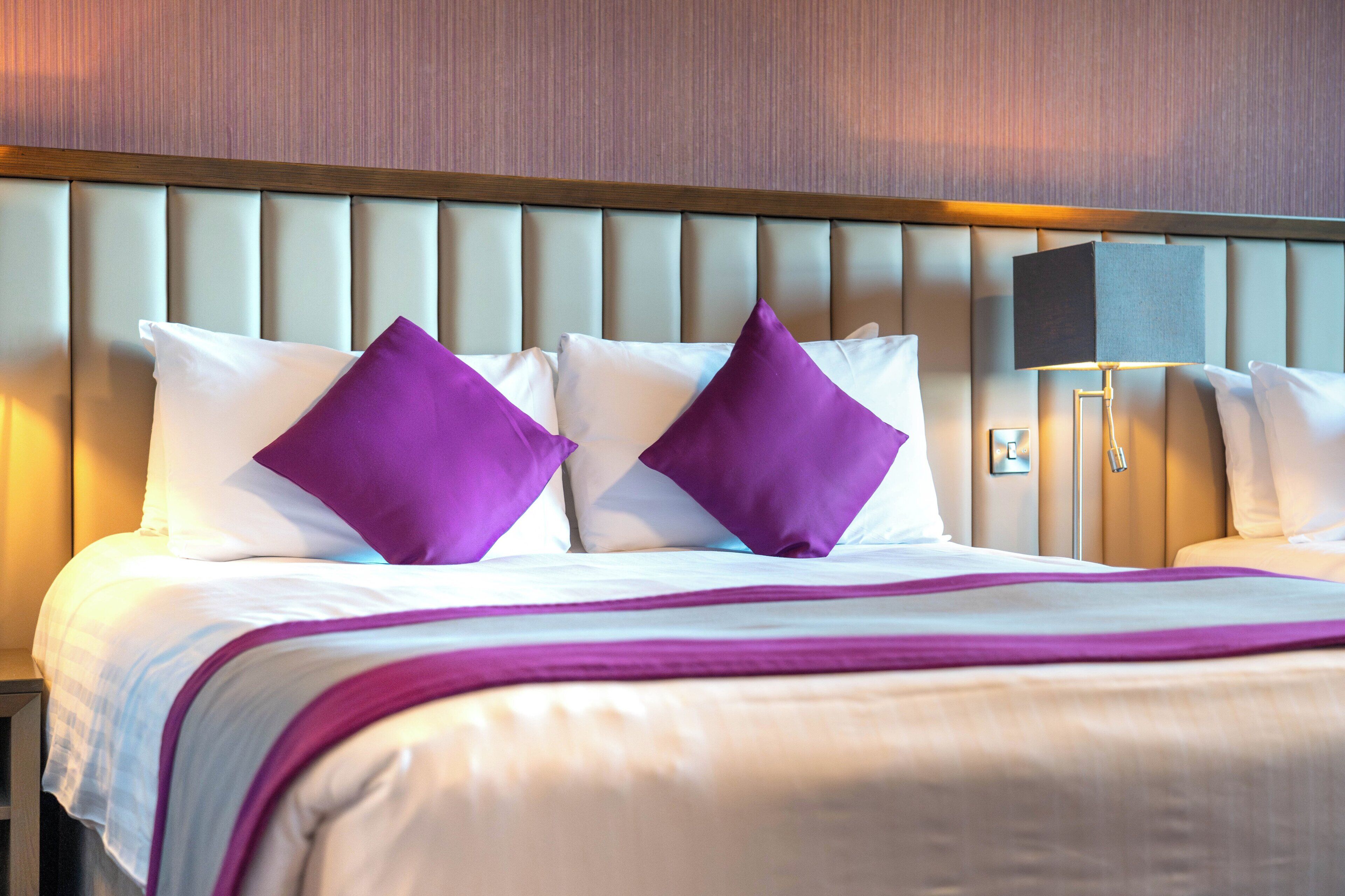 Et hotelværelse med seng, puder, et natbord og en lampe.