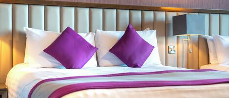 A hotel room with a bed, pillows, a nightstand, and a lamp.