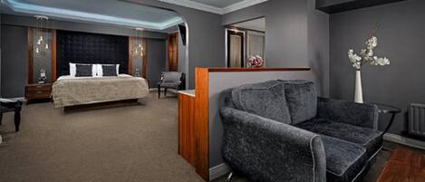Una habitación de hotel moderna con una cama grande, una zona de estar con sofá y una mesita.