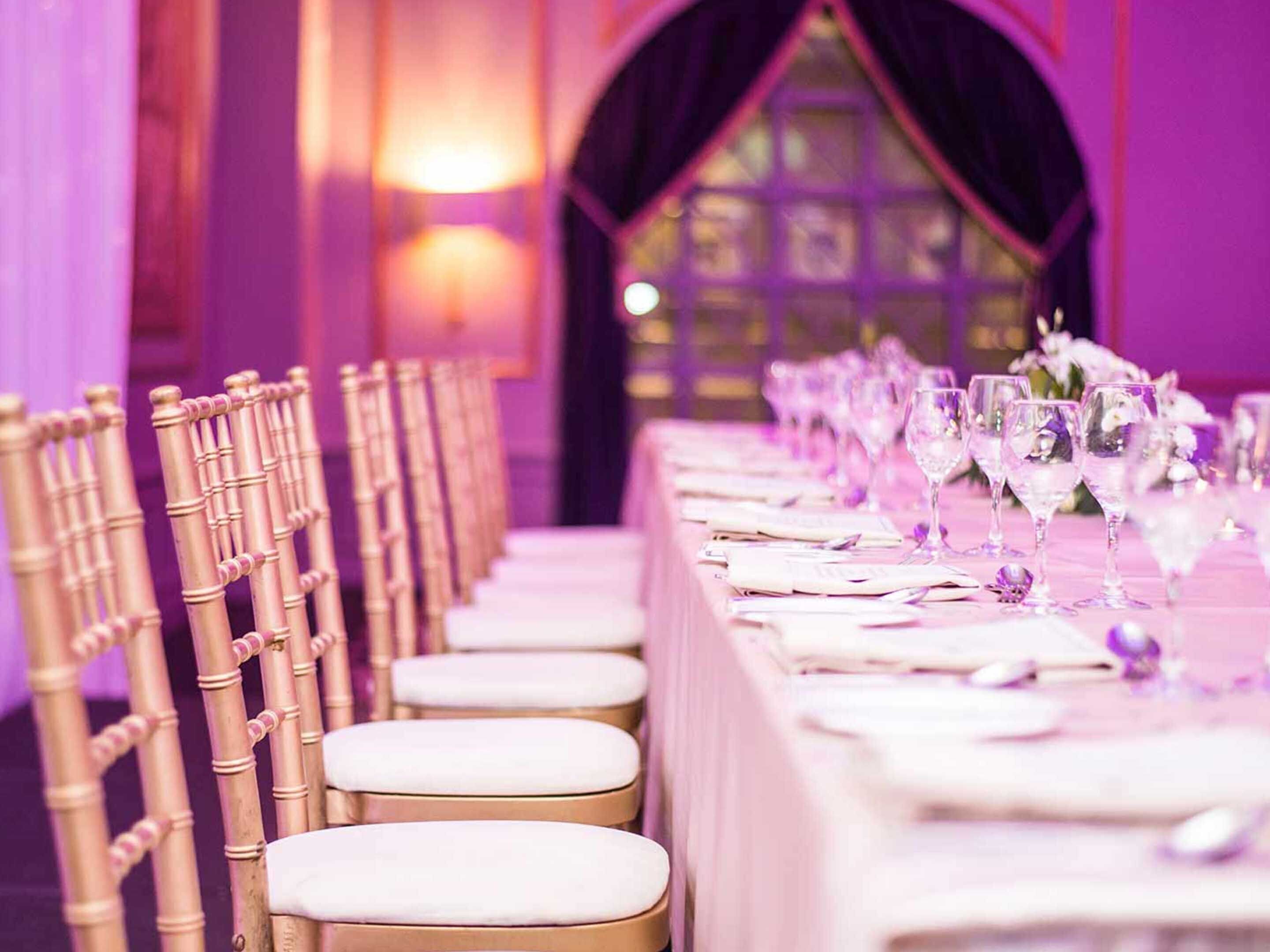 A row of bamboo chairs with white cushions and a table set with wine glasses and menus.