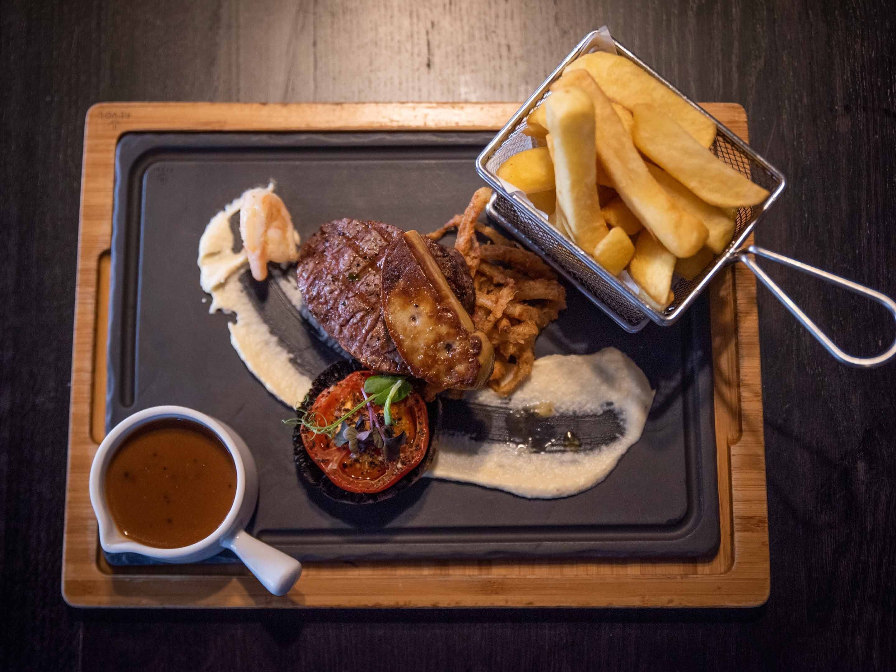 Un plato con bistec, papas fritas y una salsa acompañada, sobre una tabla de pizarra.