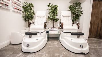 A spa room with two massage chairs, a small table, and two potted plants.