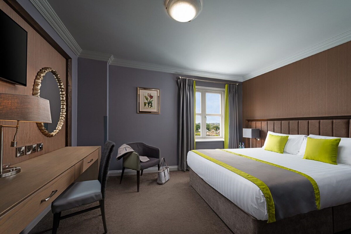 A hotel room with a bed, a desk, a chair, a TV, and a window with curtains.