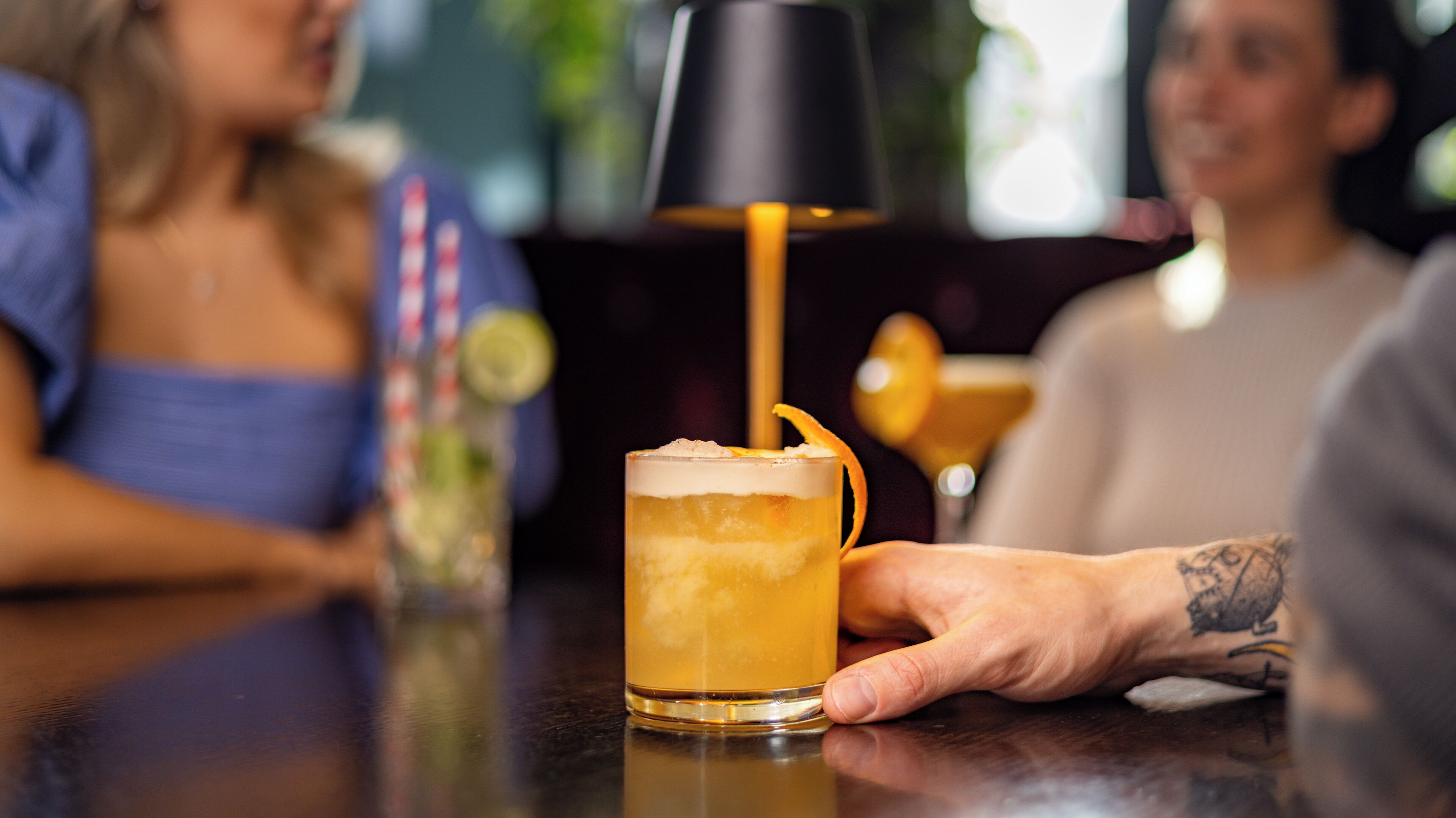 A person holding a glass with a layered drink, possibly a cocktail, at a bar.
