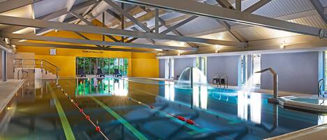 Una piscina interior con carriles claramente delimitados, un trampolín y un letrero del club de salud y bienestar.