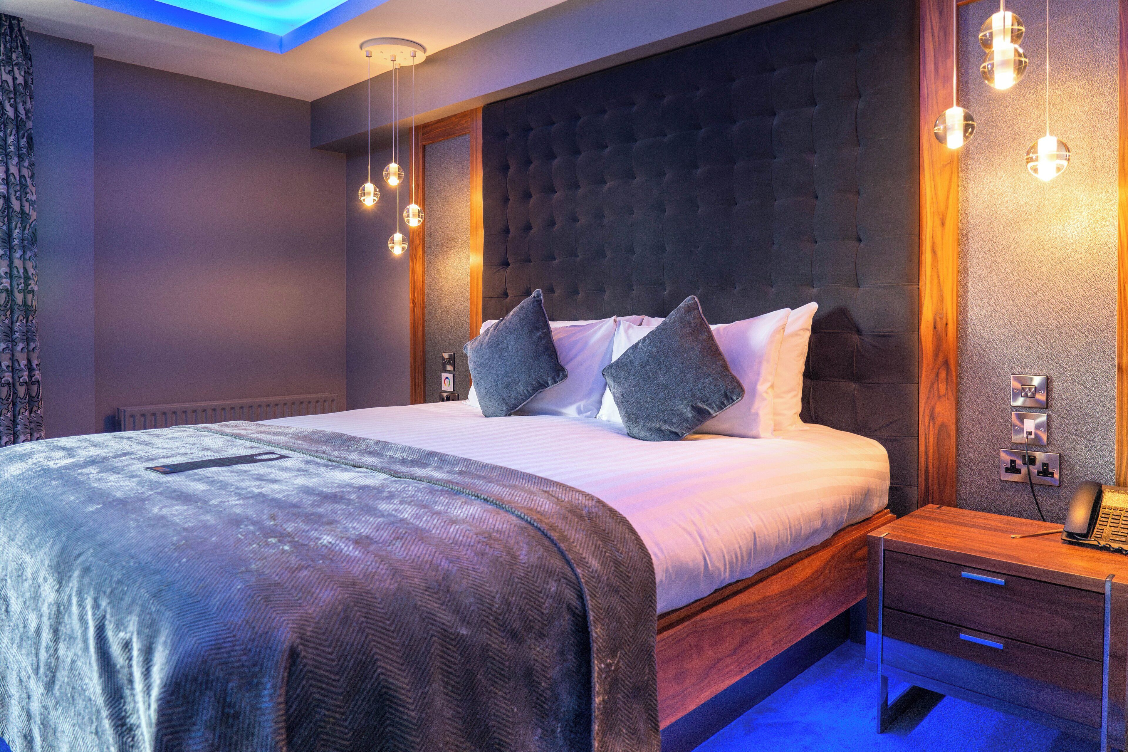 A modern bedroom with a large bed, a wooden nightstand, and a wall-mounted phone.