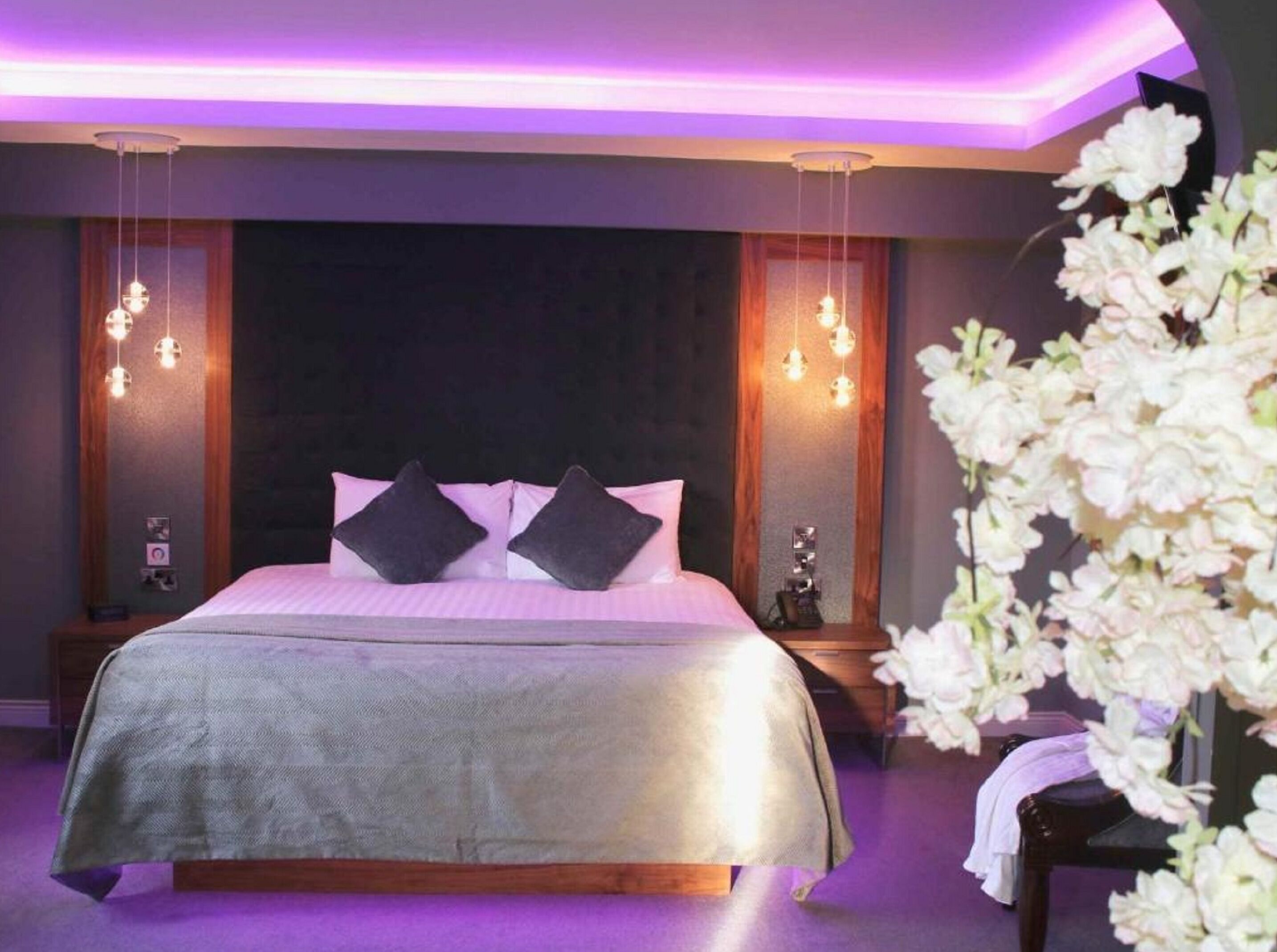 A modern bedroom with a large bed, dark walls, and pendant lighting.