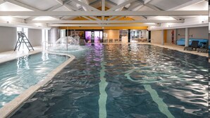 Une piscine intérieure à l’eau claire, dotée d’un plongeoir et d’un espace détente avec des chaises et une table.