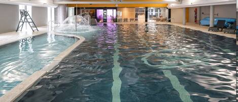 Una piscina interior con agua cristalina, un trampolín y una zona de estar con sillas y una mesa.
