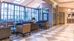 Un hall d’entrée spacieux, doté d’un sol à carreaux, de grandes fenêtres et d’un espace détente avec des canapés et des fauteuils.