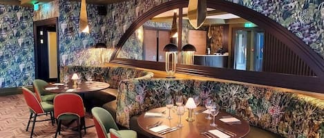 Ein Restaurant mit floralem Wandpapier, runden Tischen und Stühlen in Grün und Rot.