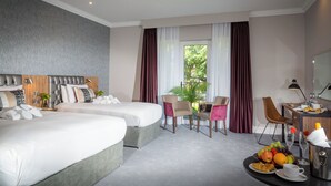 A hotel room with two beds, a dining area, a desk with a computer, and a view of greenery outside. - Talbot Hotel Midleton (Midleton)