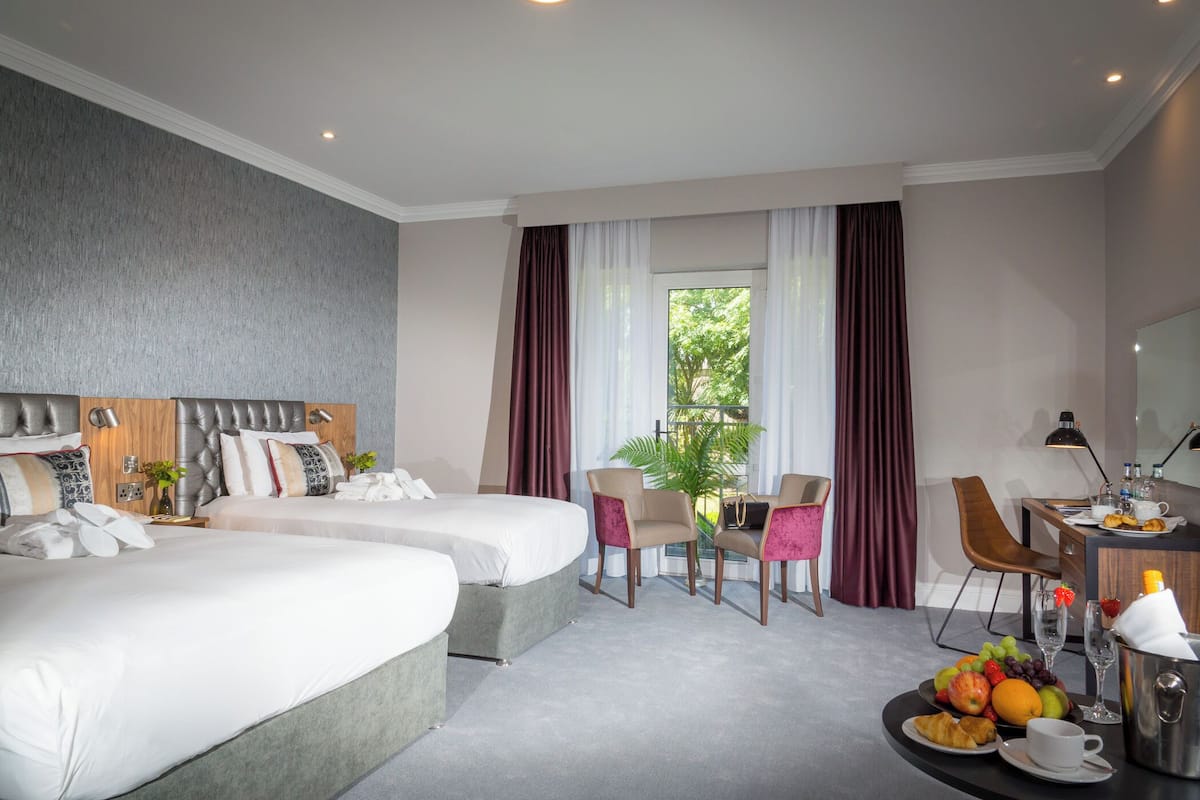 Une chambre d’hôtel avec deux lits, un coin repas, un bureau avec un ordinateur et une vue sur la verdure.