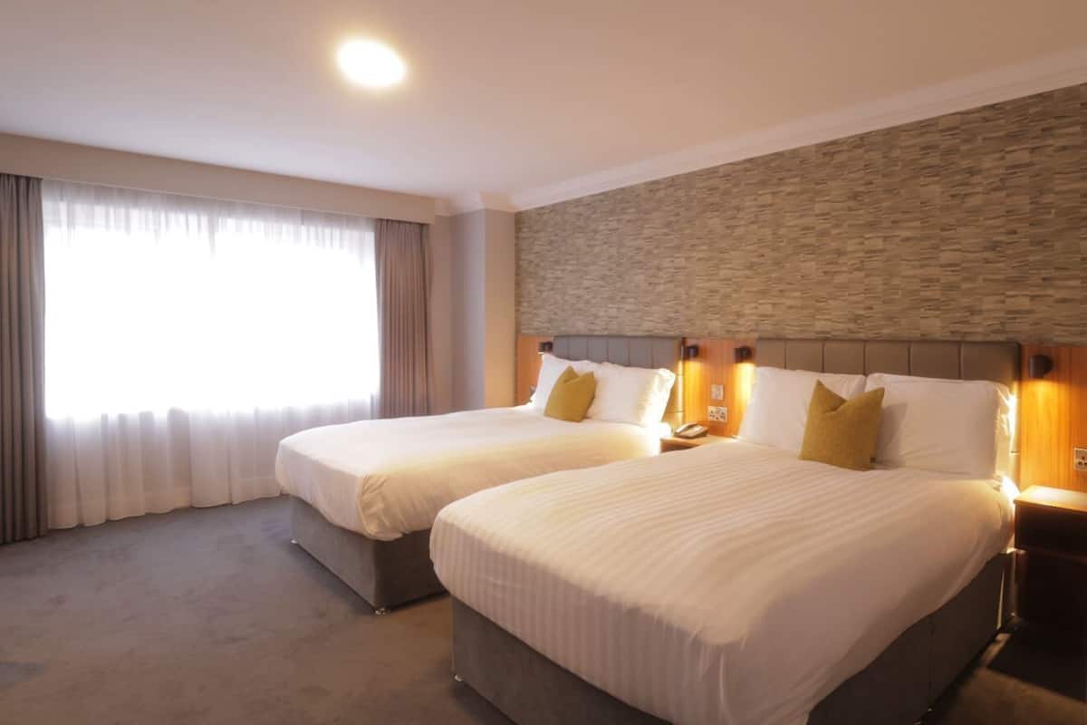 Une chambre d’hôtel avec deux lits, un mur décoratif en pierre et une grande fenêtre avec des rideaux.