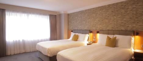 A hotel room with two beds, a stone accent wall, and a large window with curtains.