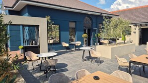 An outdoor patio with wicker chairs and tables, a building with a blue facade, and a tiled roof. - Talbot Hotel Midleton (Midleton)