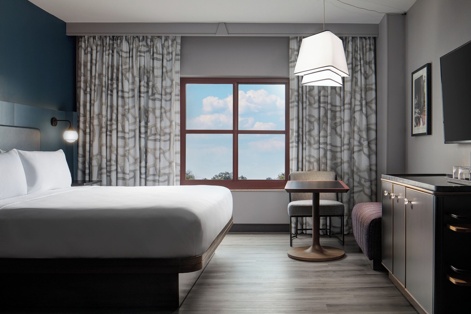 A hotel room with a bed, a small table, a chair, a desk, and a wardrobe.