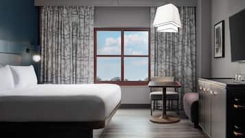 A hotel room with a bed, a small table, a chair, a desk, and a wardrobe.