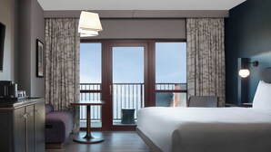 Une chambre d’hôtel avec un lit, un bureau, une chaise, une petite table et une vue sur le ciel par les portes du balcon.