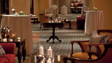 A hotel lobby with a central round table surrounded by chairs, a patterned carpet, and tables with candles and decorative items.