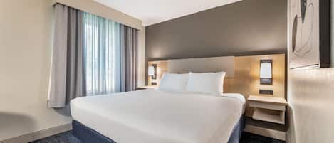 A hotel room with a large bed, a nightstand, a lamp, and a window with curtains.